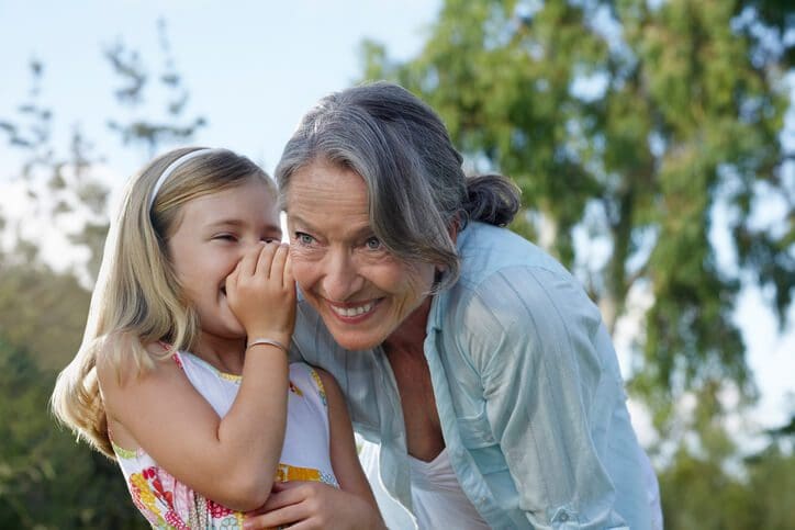 Closeup of a young girl whispering in grandmother's ear outdoors