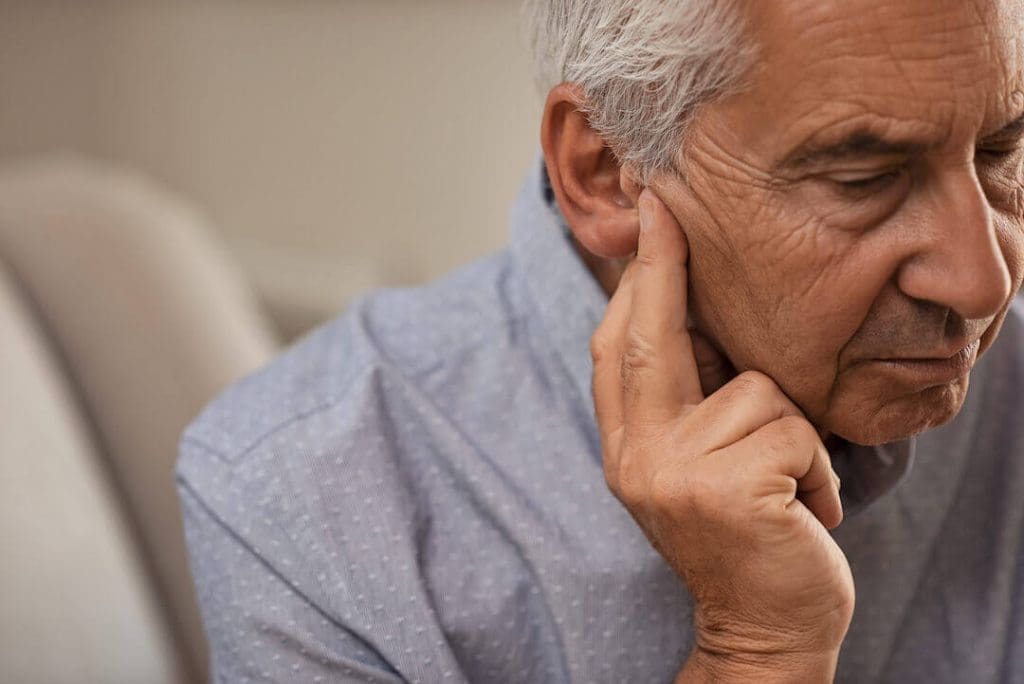 older man pressing his finger against his ear
