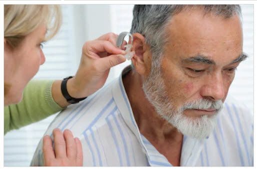 Woman fitting a hearing aid in a man's ear